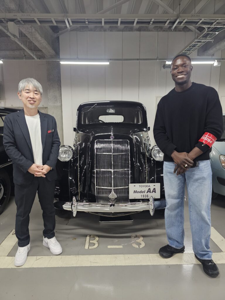 A photo taken during a tour of the Toyota Archives, featuring the founder of the Engineering Community (right) and a Toyota Museum representative (left) standing next to a 1936 Toyoda Model AA.