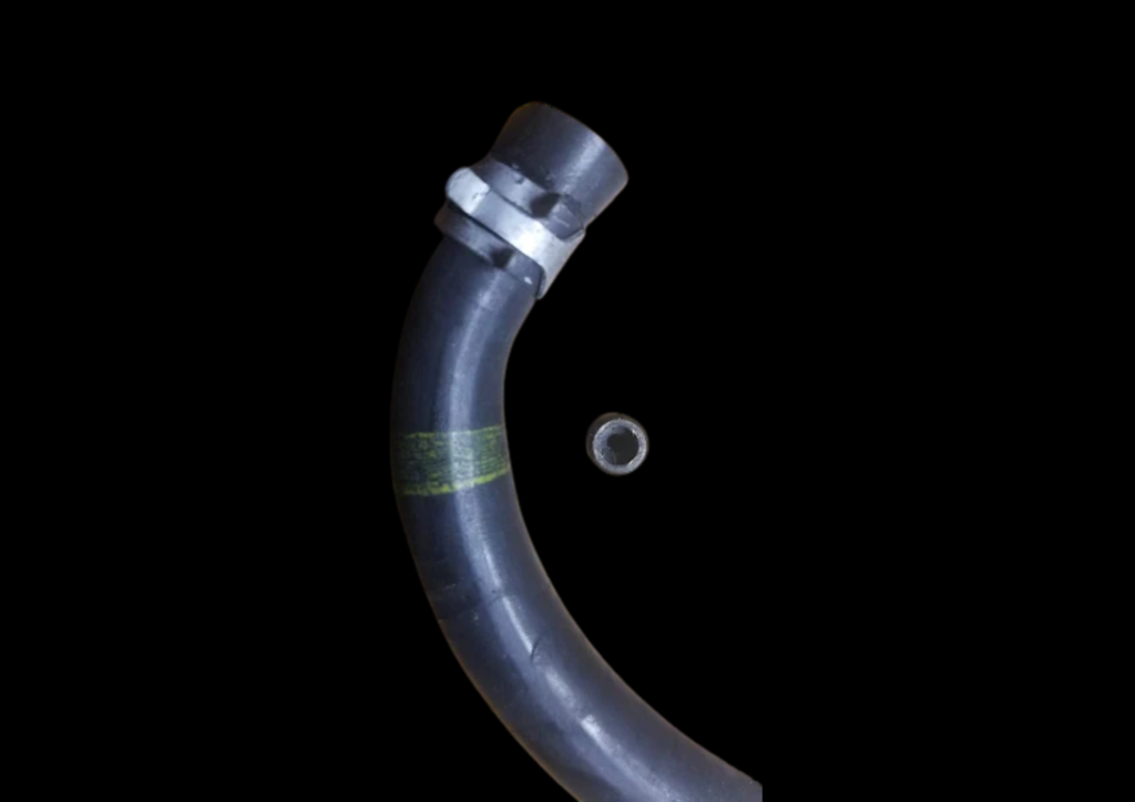 Close-up of the OEM Nissan RB26 vacuum hose with the identifying yellow paint band, shown alongside the removed brass restrictor pill